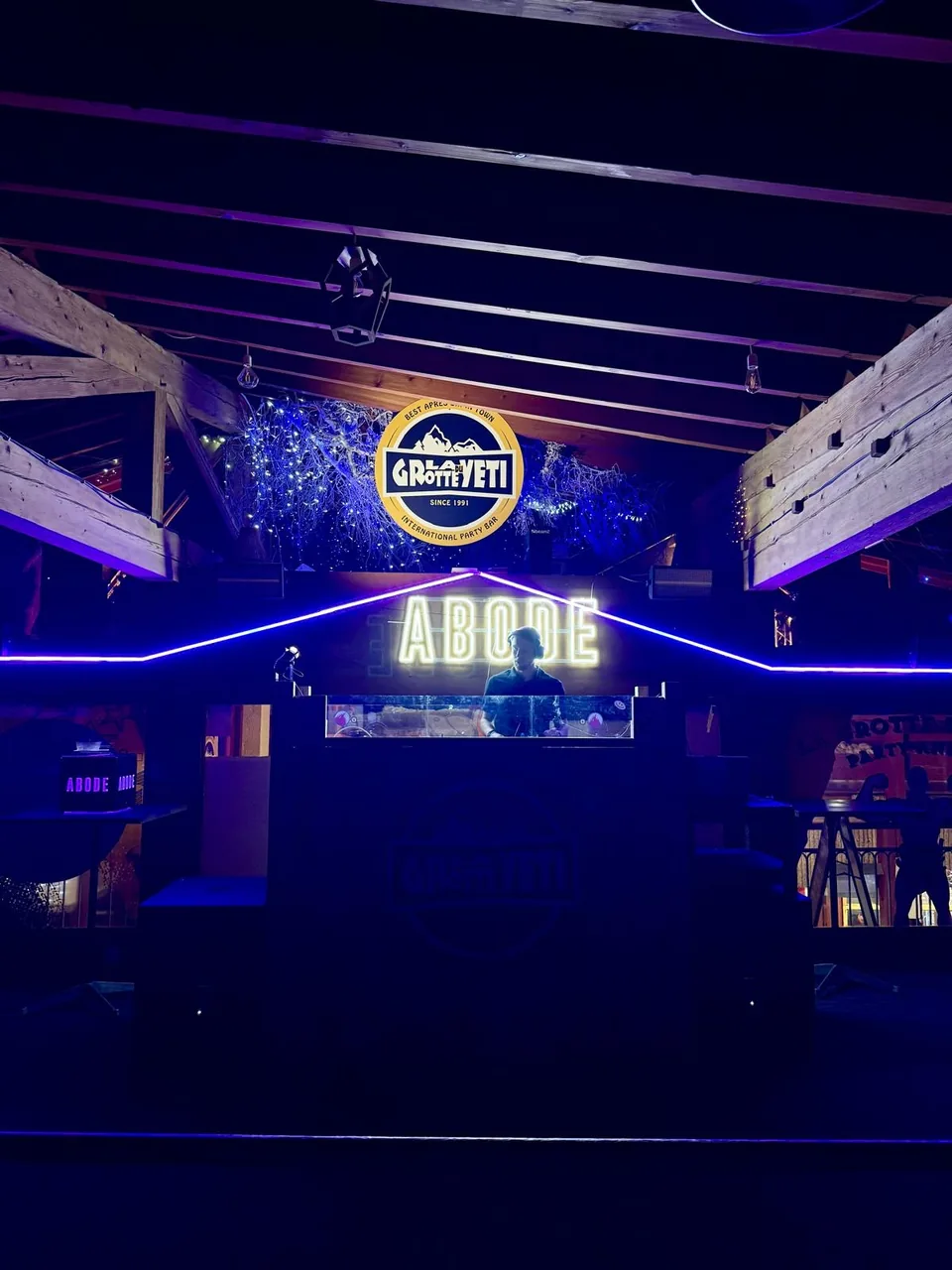 Wide view of a DJ booth with NATUS behind the decks, blue strip lighting and exposed wooden beams