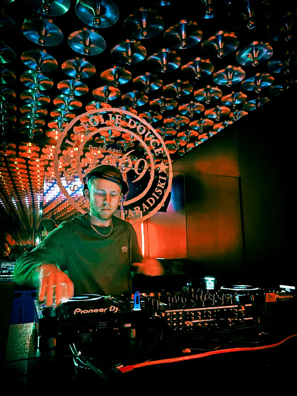 NATUS mixing on Pioneer DJ decks beneath a mirrored ceiling and colourful lights
