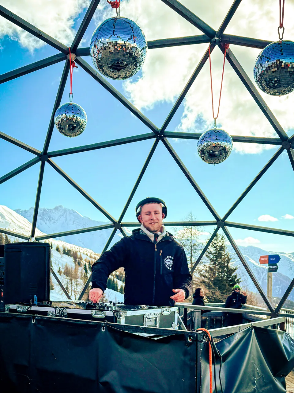 NATUS DJing beneath mirrored disco balls in a glass dome overlooking snowy mountains
